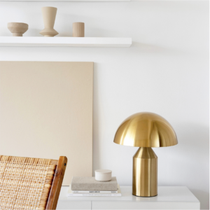 A gold lamp sitting on top of a white table in front of a white shelf with 3 vases.